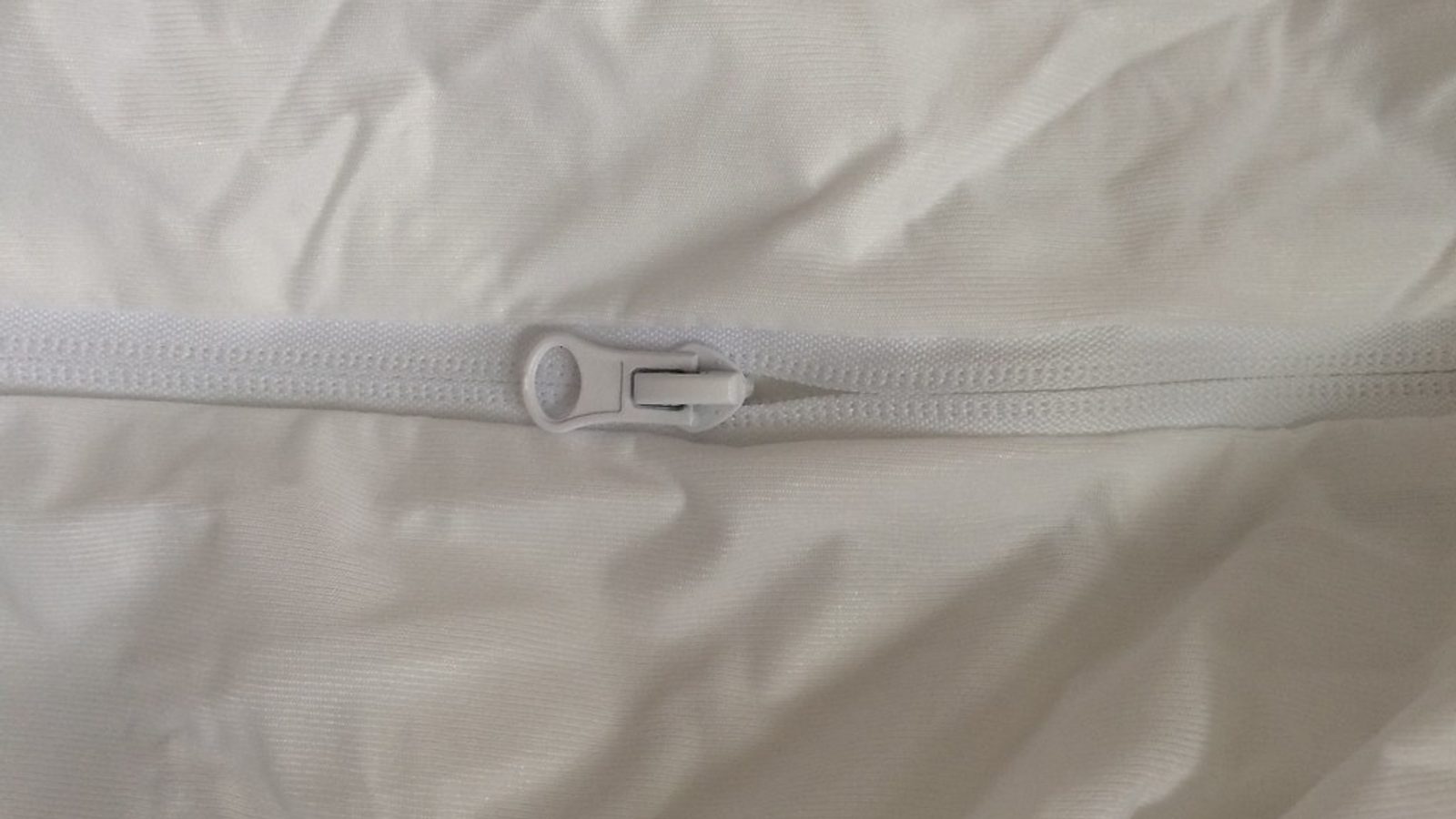 Detalhe do fecho de correr branco numa capa de encerramento de colchão anti-percevejos.