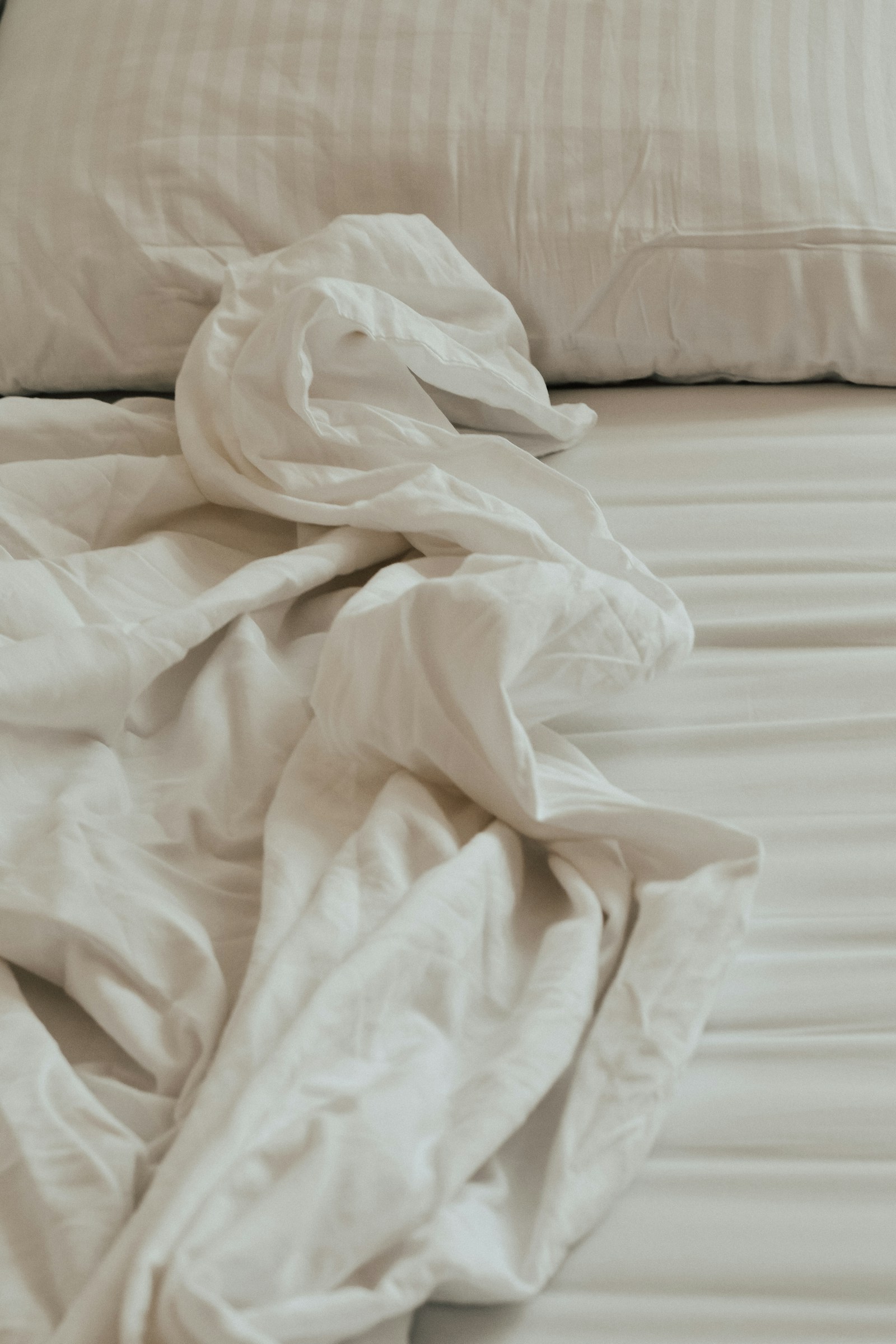 Cama com lençóis brancos amarrotados e desfeitos — primeiro passo da ordem de trabalho: retirar toda a roupa de cama.