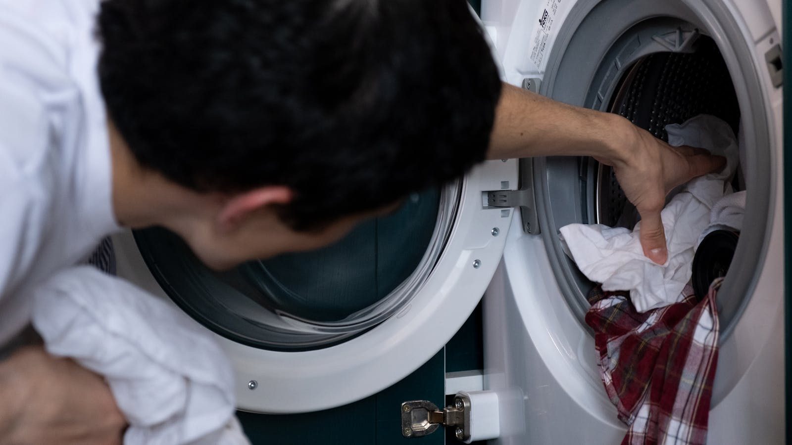 Pessoa a retirar roupa de uma máquina de lavar, com vista para o tambor aberto.