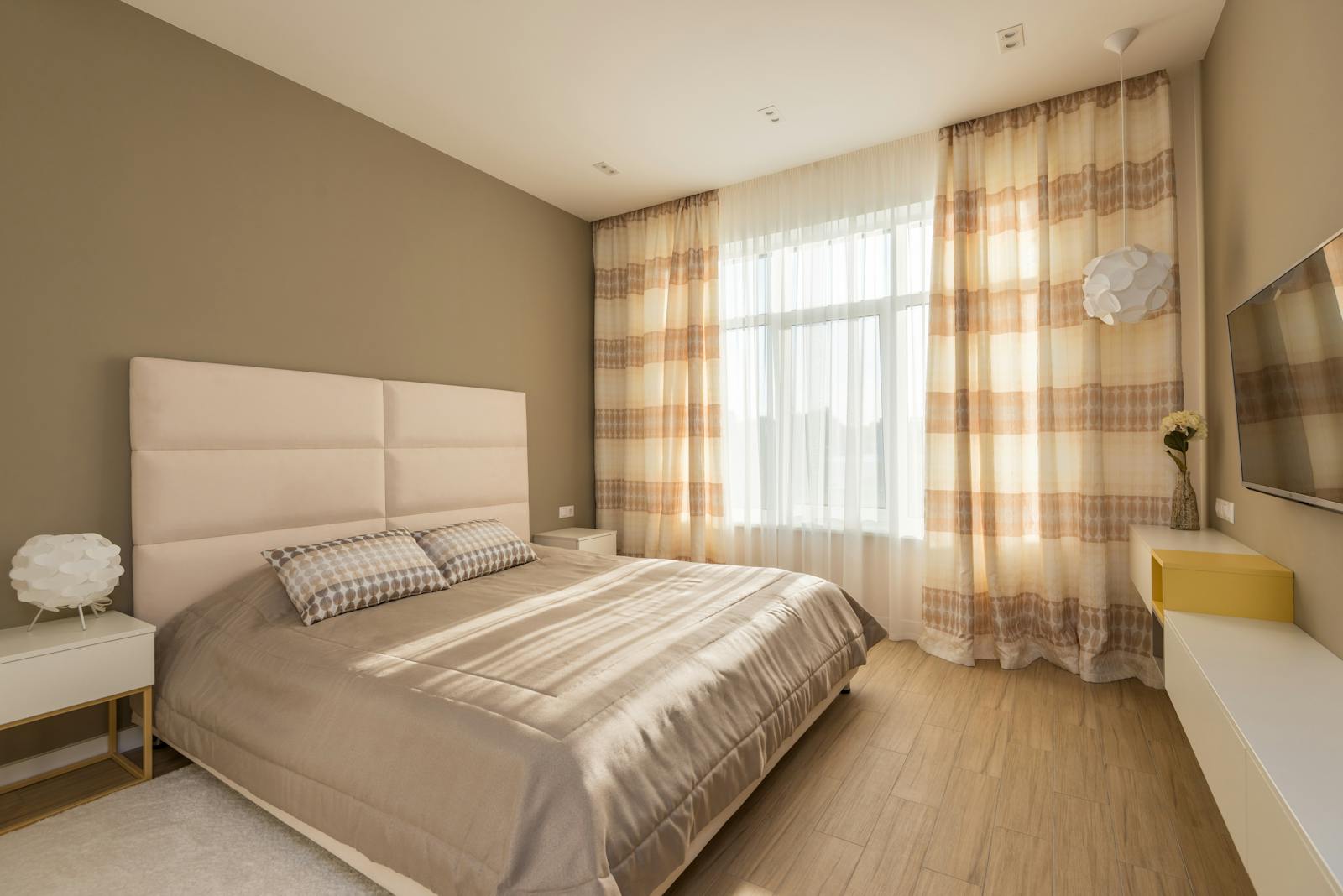 Quarto com cama, cabeceira acolchoada, cortinas até ao chão e piso em madeira — zonas onde o vapor pode ser aplicado com cuidado.