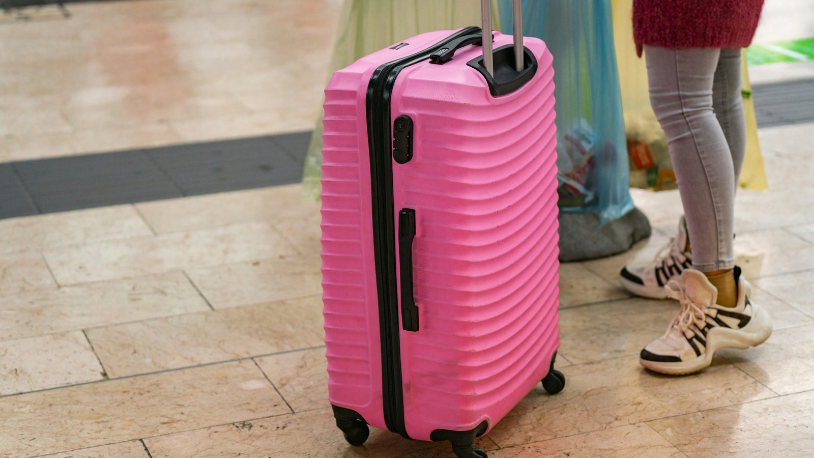 Mala de viagem cor-de-rosa pousada sobre piso de azulejo num corredor, sem tapetes nem estofos à volta.